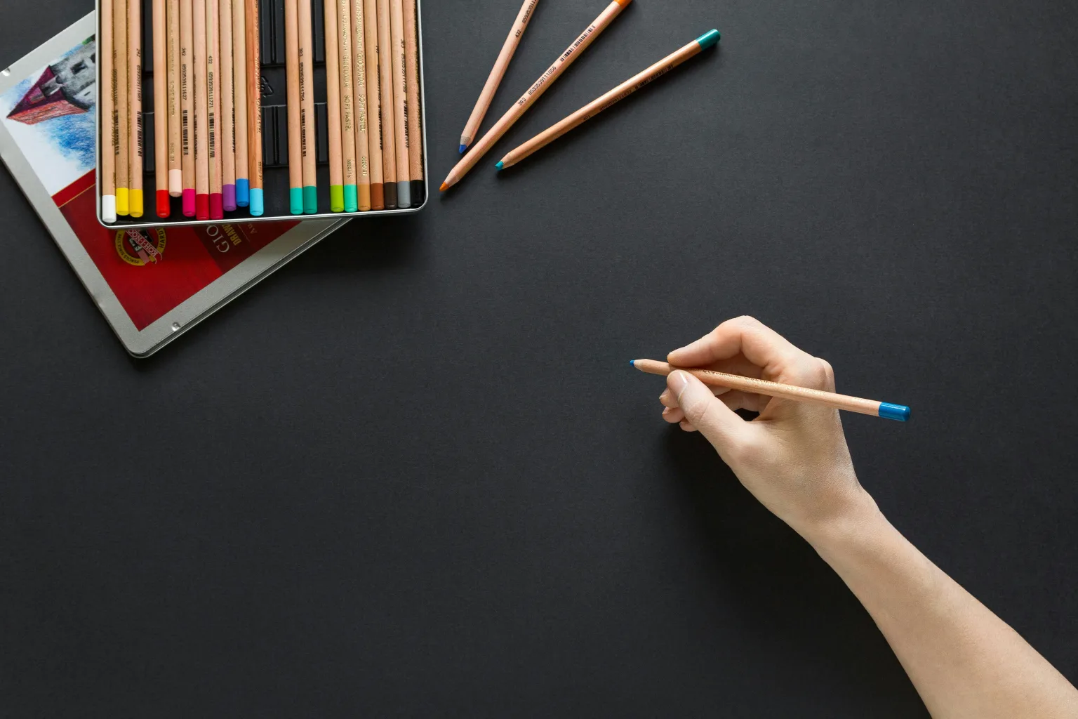 A person holding colored pencils to design a logo.
